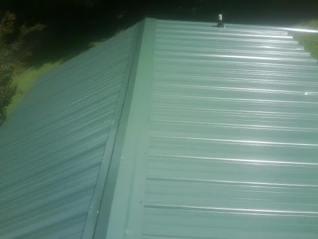 New green metal panels meeting at the ridge of a roof — Flat Roof Repair work by our crew in Cressona