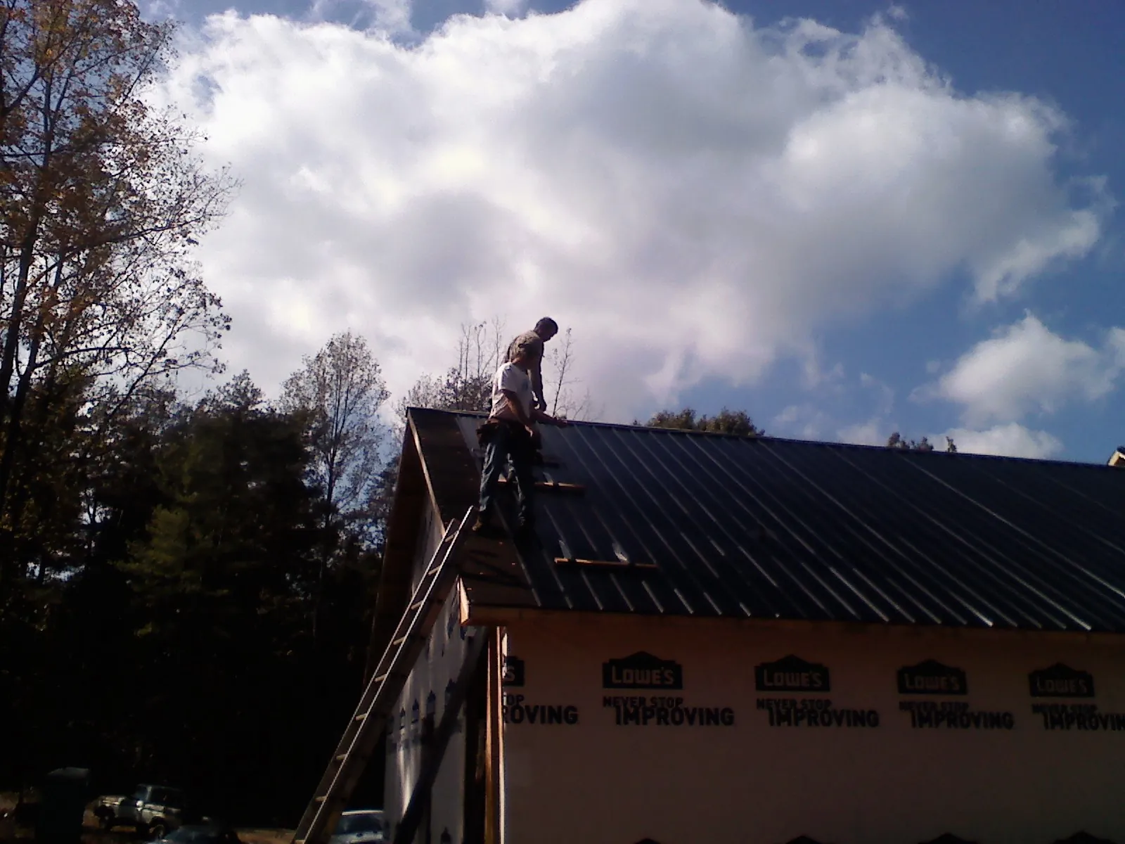 Roofer fastening dark metal panels high against a cloudy sky, from a Roof Inspection job in Cressona