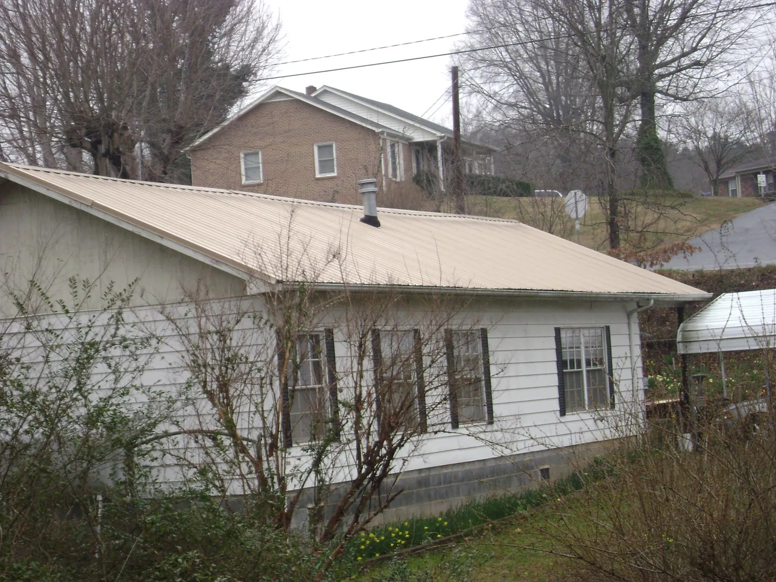 Tan metal roof on a white sided house set into a hillside — Commercial Roofing by Roofing Brothers in Cressona